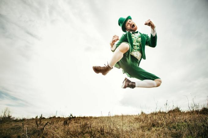 شخصية أيرلندية نمطية جاهزة تمامًا ليوم القديس باتريك يقفز ويرقص في حقل مفتوح من الجانب الأيرلندي من الريف نسخة الفضاء في السماء والعشب