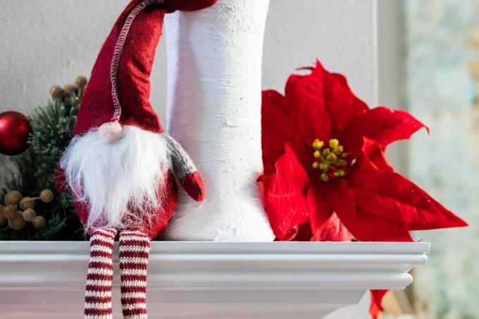 زينة جنوم كلاسيكية لعطلة عيد الميلاد النرويجية تجلس على عباءة بيضاء حديثة مع مزهرية بيضاء مع الأوكالبتوس وزهرة البونسيتة