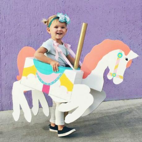 فتاة صغيرة مع صندوق على شكل ورسم ليبدو وكأنه حصان دائري حولها