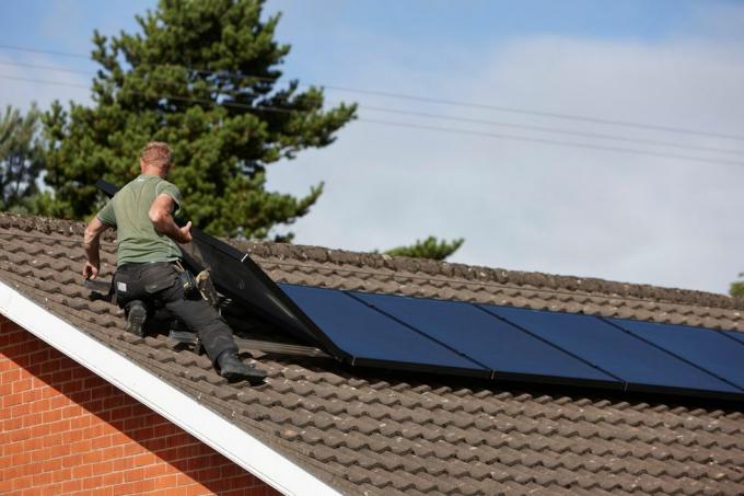 رجل h0chn1 يقوم بتركيب مجموعة من الألواح الشمسية على السطح في منشأة تركيب ألواح شمسية محلية في المملكة المتحدة