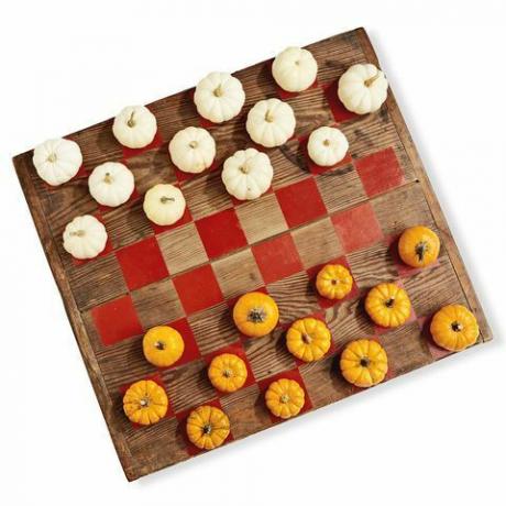 لوح خشبي مطلي مثل لعبة الداما باستخدام القرع الصغير باللونين الأبيض والبرتقالي مثل قطع اللعب