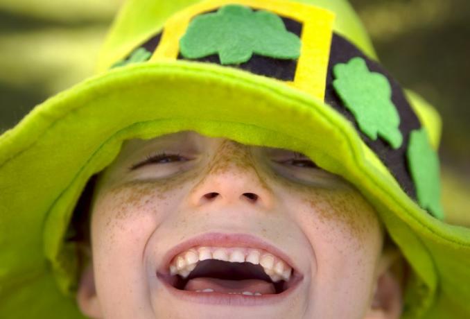 صورة مقرّبة لطفل مبتسم منمش في يوم القديس باتريك يرتدي اللون الأخضر المكسو بالنباتات ويحتاج إلى تسمية توضيحية لطيفة