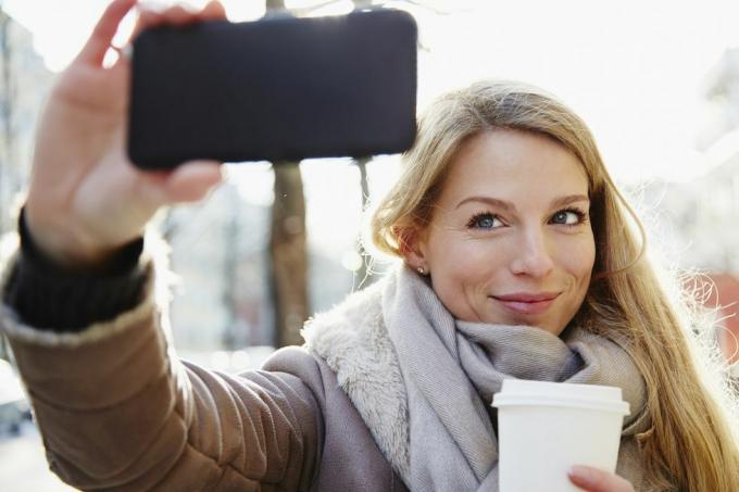 امرأة وسيم تتجول في شوارع المدينة في الشتاء وتلتقط صورة شخصية وتحمل القهوة للذهاب، بإضاءة خلفية