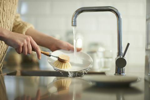 امرأة تستخدم فرشاة خالية من البلاستيك لتنظيف الأطباق في حوض المطبخ ، عن قرب