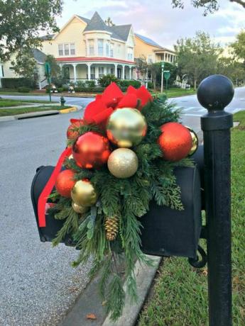 صندوق البريد الأسود والبريد المغطى بالخضرة لعيد الميلاد مع كرات عيد الميلاد الذهبية والحمراء ، وكوز الصنوبر وقوس أحمر مخملي