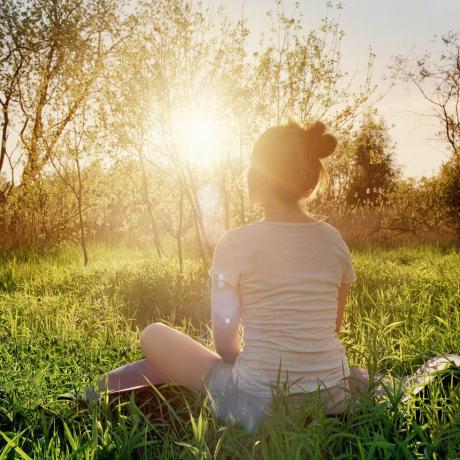 امرأة شابة تجلس في وضع اليوغا وتستمتع بغروب الشمس في الطبيعة