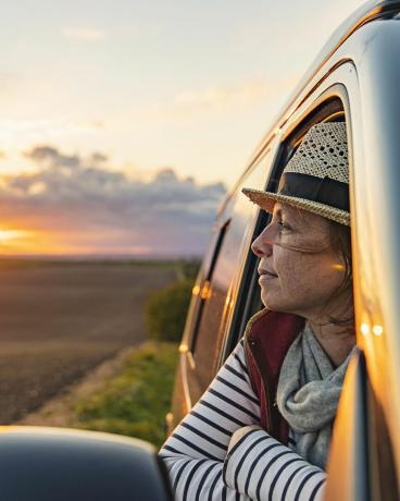 امرأة في الأربعينيات من عمرها تنظر إلى الريف من شاحنتها، وتبدو راضية ومرتاحة