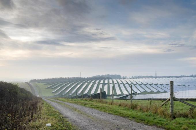 موقع للطاقة الشمسية يقع في قلب الريف الإنجليزي، محاط بسياج، ويمتد بجواره مسار ترابي ضيق إلى الأراضي الزراعية